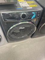 Front-loading Electrolux washing machine with protective plastic wrap and blue tape, energy guide labels on top.