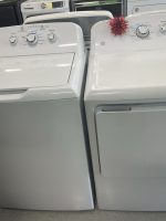 Row of white top-load washing machines on display in a showroom, with dial controls and a small yellow price tag