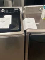 Two Samsung washing machines on display in a showroom, one top-load with a glass lid on the left.