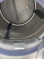 Interior view of a front-loading washing machine drum with a perforated central panel and three black handles around the rim