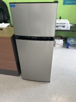 Stainless steel Frigidaire two-door refrigerator in an office, placed beside a wooden desk against a green wall.