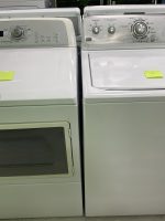 White Maytag front-loading dryer beside a white top-load washer, each with a yellow note on the lid in a showroom setting