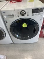Front-loading LG washing machine on display with a large central dial and control panel, yellow sticky note on the door.