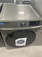 Front-loading Samsung washer/dryer unit in a showroom with a large circular control dial on the front panel; a sale sign on the door reads '$625' and there is a blue 'NEW' sticker on the left side.