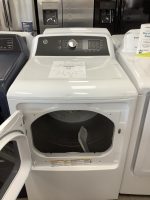 White top-loading washing machine in a showroom with its lid open and a sale price sheet on the top surface (says 'SALE PRICE $295').