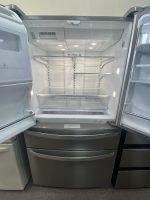 Open stainless steel refrigerator with bottom freezer drawers; interior shelves are empty and lights are on in a modern kitchen unit.