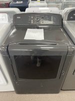 Gray top-loading clothes dryer in a showroom with a sale price sign on the lid edge and visible control panel at the back.