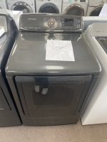 Samsung dark gray top-loading washing machine in a showroom, sale sign on the lid reading 'SALE PRICE $295'