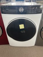 White front-loading washing machine on display with a black-tinted door; a yellow sticky note is attached to the door.
