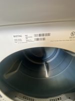 Front-loading washing machine drum with a white label showing Maytag branding and a barcode on the rim.