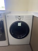 Front-loading washing machine in a laundry room against beige walls, with a small sticky note on the door.