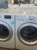Two front-loading washers in a showroom with control panels and circular doors, with more laundry machines visible in the background.