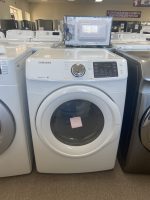 Front-loading Samsung washing machine in a showroom, with a microwave placed on top of the unit.