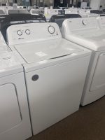 White top-load washing machines on display in a showroom with sale tag visible in the foreground, row of machines behind them.