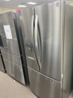 Row of stainless steel refrigerators in a showroom, with price tags visible on the doors and labels nearby.