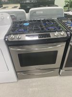 Stainless steel Frigidaire gas range with five burners on a showroom display counter, digital controls on top panel.
