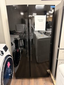 Black side-by-side refrigerator with a built-in water/ice dispenser on the left door and a sale sign reading 'Sale Price $295.00' on the right door in a showroom.