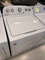 Whirlpool front-loading washer with control dial and settings, beside a matching dryer with a yellow note on its door