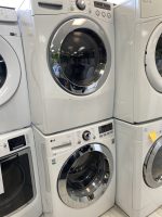 Row of white front-loading washing machines and dryers on display in a showroom.