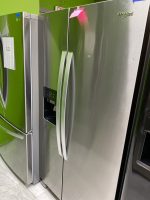Stainless steel side-by-side refrigerators on a showroom floor with a bright green wall and a Whirlpool logo visible on the right.