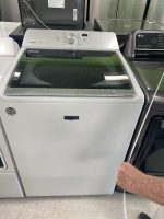 White Maytag Bravos XL top-load washer on display in a showroom, control panel visible above the lid.