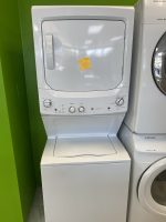 Stacked white washer and dryer against a bright green wall, with a yellow sticky note on the top dryer door.