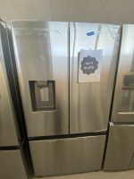 Stainless steel side-by-side refrigerator with a left water dispenser; a sale sign taped to the right door reads $1,275.