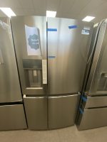 Stainless steel side-by-side refrigerator in a showroom with a sale sign reading 'Sale!! $1,495' taped to the left door.