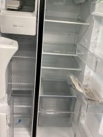 Two side-by-side open refrigerators, mostly empty, with shelves and door bins visible. Left unit shows an ice maker; right unit is a standard fridge with multiple shelves and a shallow crisper drawer at bottom.