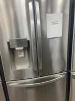 Stainless steel side-by-side refrigerator with water dispenser and a sale price note reading $995 taped to the door.