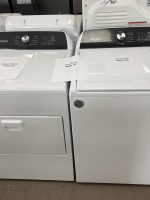 Two white Whirlpool top-loading washing machines on a showroom floor with sale papers displaying prices (e.g., $450.00, $895.00).