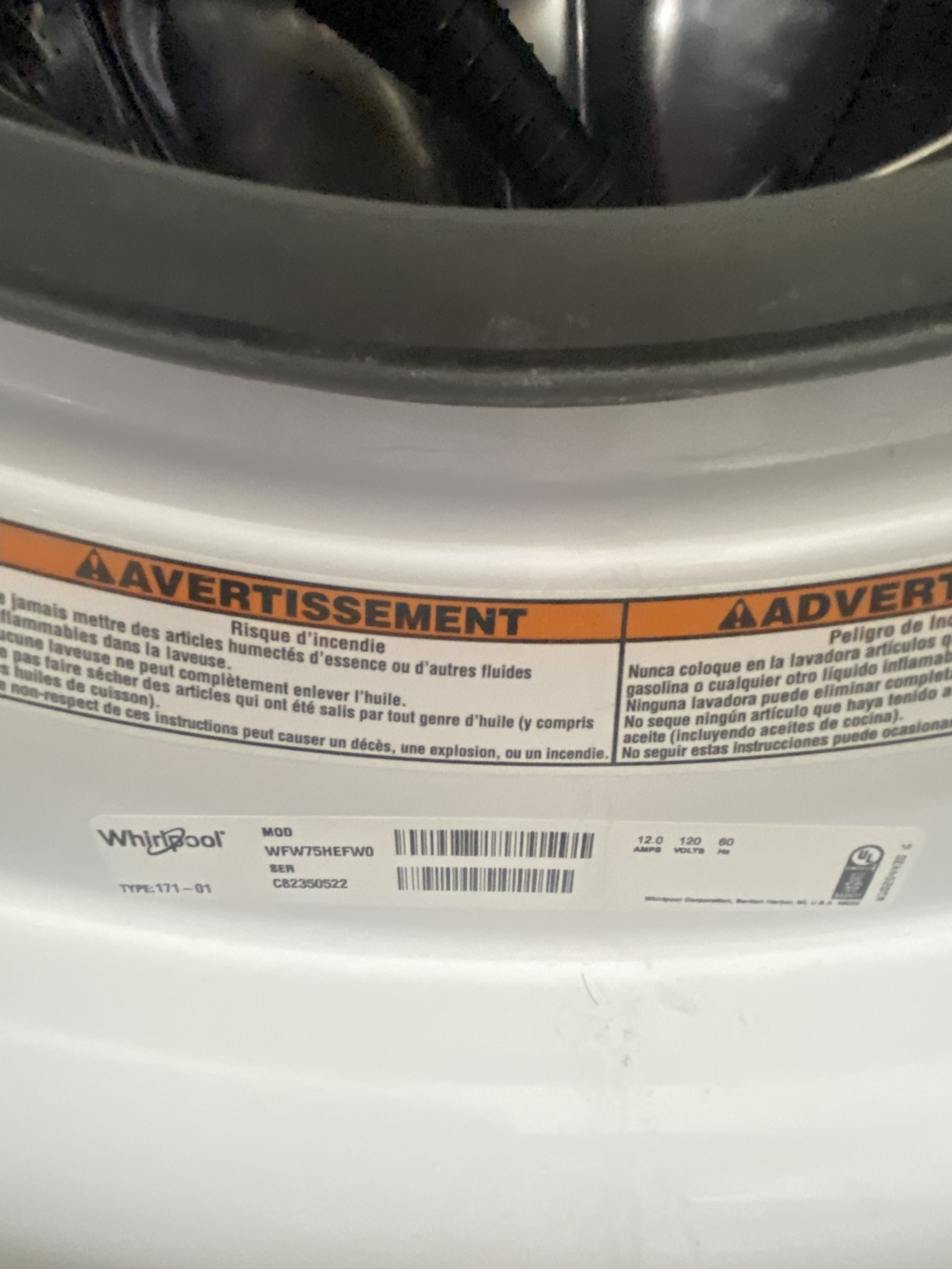 img_6189 - Discount Appliances Close-up of a washing machine drum with an orange warning label and barcode sticker (Whirlpool) visible on the front panel.