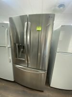 Stainless steel LG French-door refrigerator with a water dispenser in a showroom; sticky note on the door.