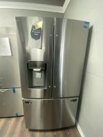 Stainless steel French-door refrigerator with water dispenser and price note taped to left door, in a showroom corner