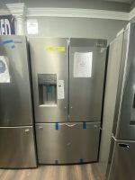 Three stainless-steel refrigerators lined up in a showroom, with a sale price sign on the middle door and blue tape marks on the bottoms.