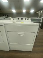 Front-to-back row of white top-loading washing machines in a showroom, wooden floor, fluorescent ceiling lights above.