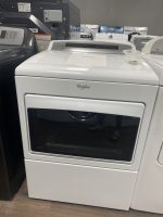 White Whirlpool front-loading washing machine on display in a showroom, with a small clear plastic container on its top and other appliances visible in the background