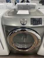 Samsung front-loading washing machine with a glass lid open, chrome door, and control panel on the right in a showroom. A sale price tag rests on top.