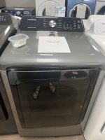 Samsung top-load washing machine on a showroom floor with a sale price sign reading $295.00 on the lid area, plus a small plastic container nearby.
