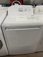 White top-load washing machine with a sale price card on the lid reading $295.00 and a small plastic container nearby in a showroom.