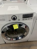 White front-loading washing machine in a retail showroom with a price tag on top and a yellow sticky note reading $325 on the door opening area. The adjacent dryer is visible on the right.