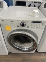 Front-loading LG Tromm washing machine on display; sale price $195.00 on a sheet beside a small plastic container with folded items.