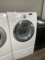 Two white front-loading laundry machines side by side in a showroom, with a paper sheet resting on top of the left unit.