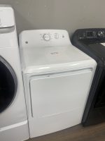 White top-loading washing machine with a circular control dial and price tag on the lid, flanked by a dryer and a dark washer.