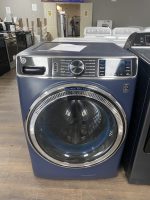 Front-loading GE washing machine in a showroom, blue base with a large circular door and control panel on top-left.