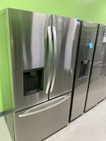 003d8c37-6386-4926-9f23-5547772e6a82-34367-0000040a72841459_file - Discount Appliances Stainless steel French-door refrigerator with water dispenser, set against a bright green wall in a showroom.
