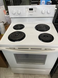 White Whirlpool electric range with four coil burners and a central digital clock in a showroom.