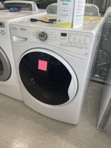 White front-loading washing machine in a showroom, pink sticky note on the door.