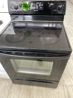 b03c4309-ca69-4eb9-aab4-e5d6e5b66afd-34024-00000c7dc0fb8322_file - Discount Appliances Electric range with a glass-ceramic cooktop; a green decorative scrubber sits on the control panel above the oven door.