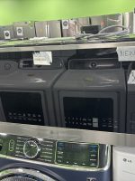 d8752e63-b1d0-4f23-bb9b-10f41278e8f1-4829-0000021b79474838_file - Discount Appliances Stainless steel LG washer and dryer set on display in a showroom with a bright green wall and price tags visible on the machines.